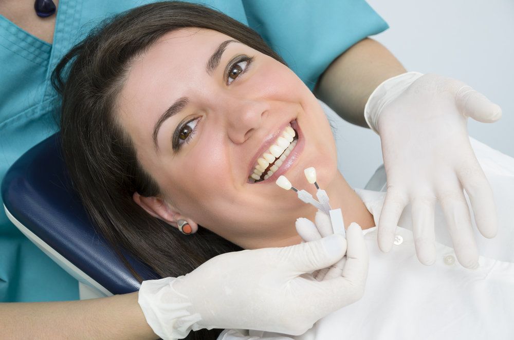 Hygienist holding shade samples up to smiling female patient's teeth